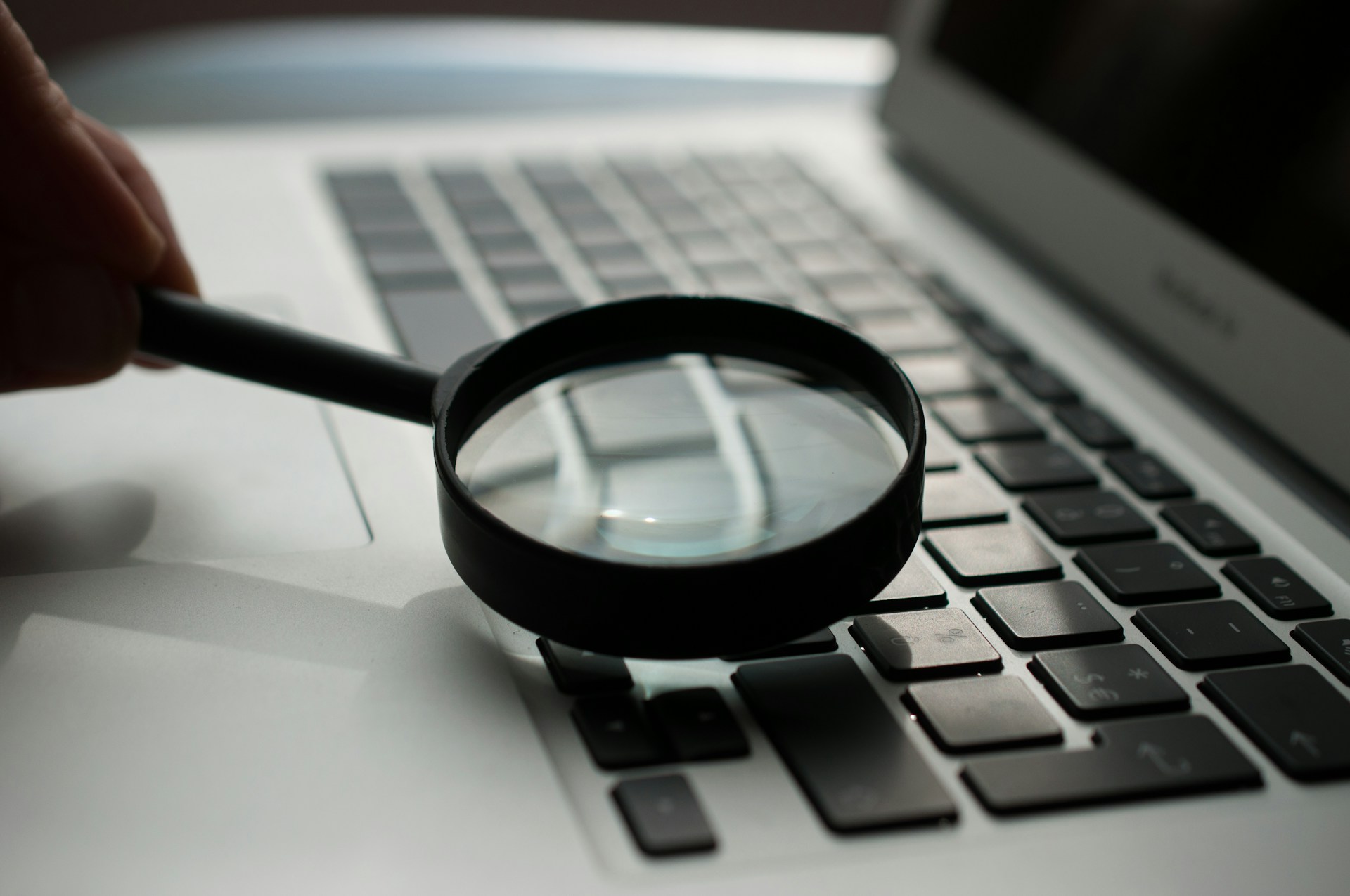 Magnifying glass held over a laptop keyboard, representing close inspection of a website for accessibility issues.